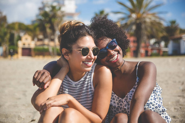 Two best female friends sitting together on beach smiling - Zdjęcie, obraz