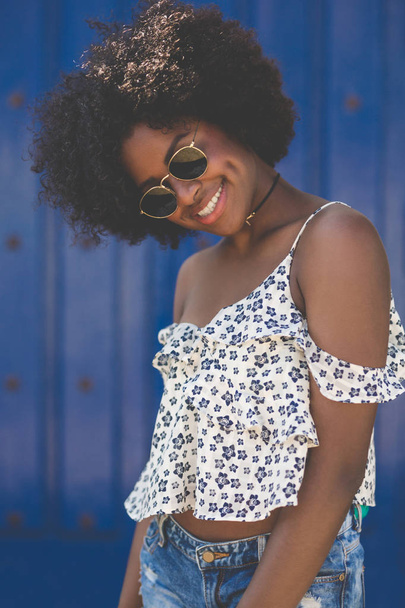 Happy afro american woman on blue background tilting head - Φωτογραφία, εικόνα