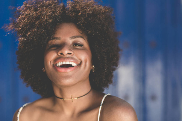 Mooie afro Amerikaanse vrouw lachen op blauwe achtergrond - Foto, afbeelding