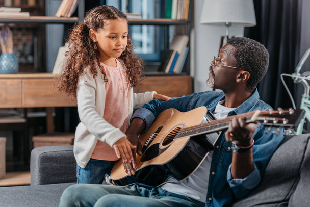 hombre tocando la guitarra con su hija en casa
 - Foto, Imagen