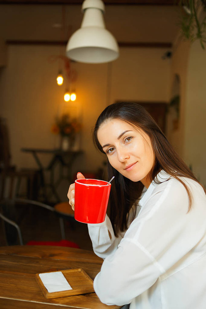 Red cup of coffee in the hands of a beautiful smiling girl - Foto, Imagen