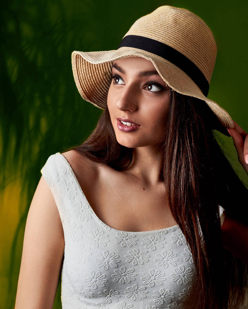 Beautiful young girl with brown eyes in hat. summer fashion beauty model girl.Studio portait closeup.Tropic green bakcground - 写真・画像