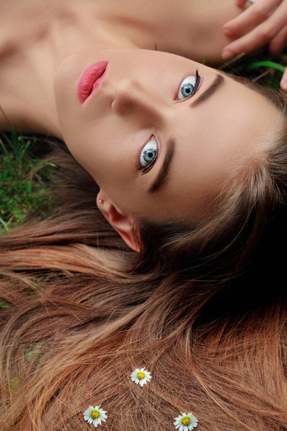 Over head close up beauty portrait of an attractive young girl with elegant long shiny hair with small camomile. Beauty in nature. Nature and beauty. Blue eyes. Concept hairstyle - Foto, Imagem