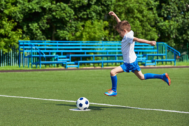 Menino jogador de futebol correndo com bola no gramado verde
 - Foto, Imagem