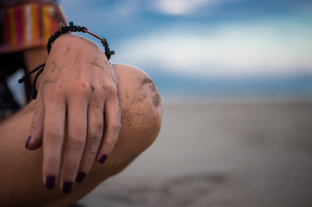 Девушка, сидящая на пляже, фокусируется на руке и колене. Овьедо
 - Фото, изображение