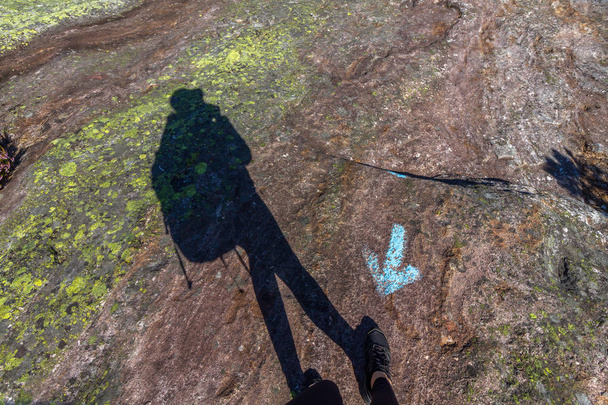Ανθρώπινη σκιά περπάτημα προς λάθος κατεύθυνση, έναντι μπλε βέλος πάνω σε βράχο - Φωτογραφία, εικόνα