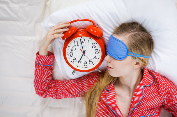 Sleeping woman wearing pajamas holding clock - Zdjęcie, obraz