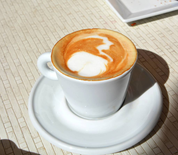Cappuccino espumoso delicioso em uma xícara branca em uma chapa
. - Foto, Imagem