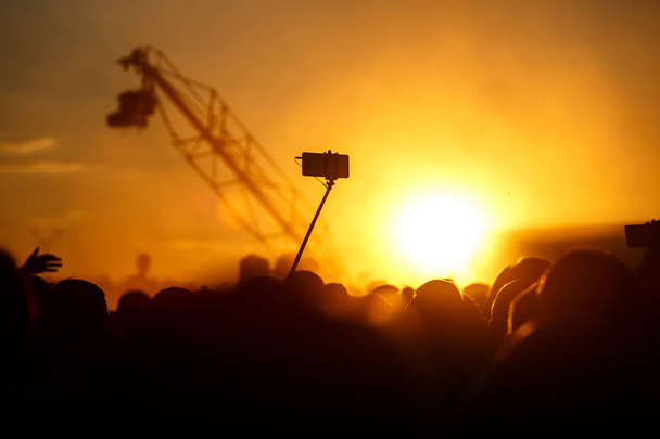 Смартфон на самоклеючій паличці, літній музичний фестиваль на заході сонця
 - Фото, зображення