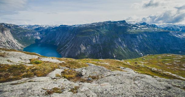 A vibrant picture of famous norwegian hiking place - way to trolltunga, the trolls tongue, rock skjegedall, with a tourist, and lake ringedalsvatnet and mountain panoramic scenery epic view, Norway - Valokuva, kuva