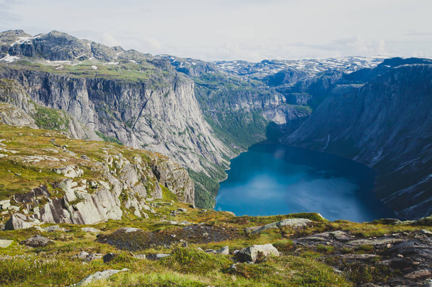 A vibrant picture of famous norwegian hiking place - way to trolltunga, the trolls tongue, rock skjegedall, with a tourist, and lake ringedalsvatnet and mountain panoramic scenery epic view, Norway - Фото, изображение
