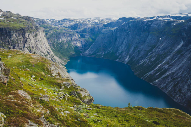 A vibrant picture of famous norwegian hiking place - way to trolltunga, the trolls tongue, rock skjegedall, with a tourist, and lake ringedalsvatnet and mountain panoramic scenery epic view, Norway - Photo, Image