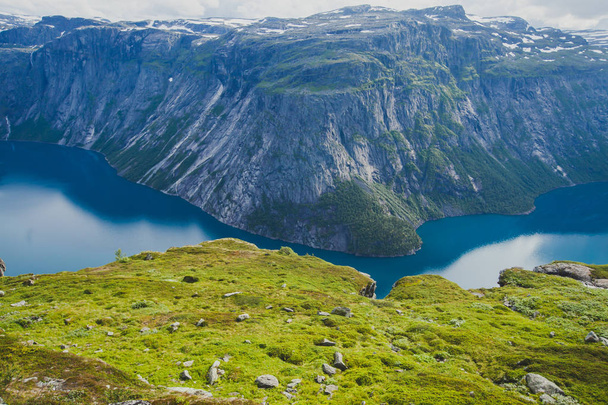 A vibrant picture of famous norwegian hiking place - way to trolltunga, the trolls tongue, rock skjegedall, with a tourist, and lake ringedalsvatnet and mountain panoramic scenery epic view, Norway - Фото, зображення