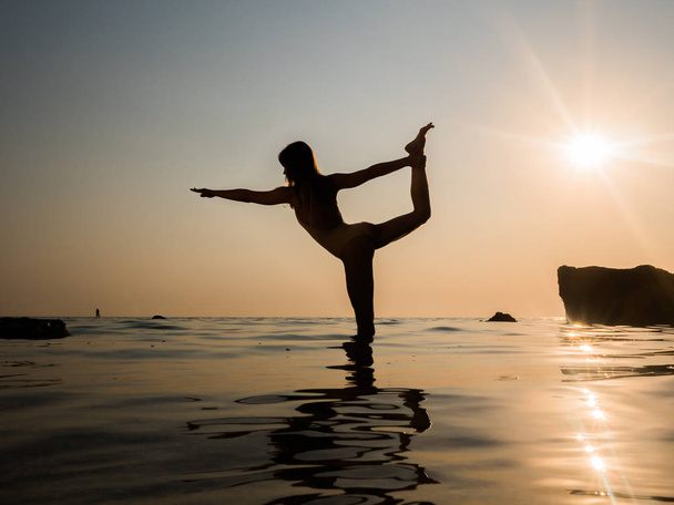 Young caucasian woman in swimsuit practicing yoga in water sea or oceanr. Beautiful reflection. Complex asanas, balance. Fitness, sport, yoga and healthy lifestyle concept. - Photo, Image
