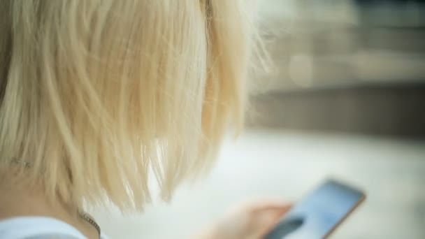 Jonge blonde vrouw in het park, maakt gebruik van een smartphone, internet, tekst, kijkt rond rustig terug weergave - Video