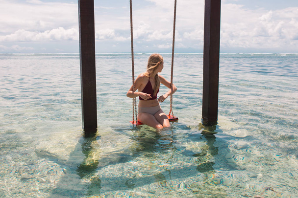 young beautiful woman on wooden swing in sea water  - Photo, Image