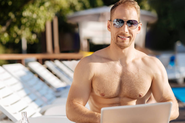 Good-looking man in sunglasses posing while working on laptop - Fotó, kép