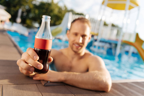 Young man showing a soda while being in swimming pool - Fotoğraf, Görsel