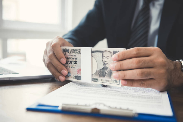 Empresário segurando dinheiro, contas de iene japonês, na mesa de trabalho
 - Foto, Imagem