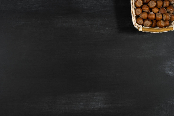 Hazelnuts in a basket on a black board.  - Фото, изображение