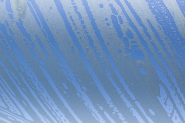 Sapone detergente espanso su un vetro trasparente. Fondo blu
. - Foto, immagini