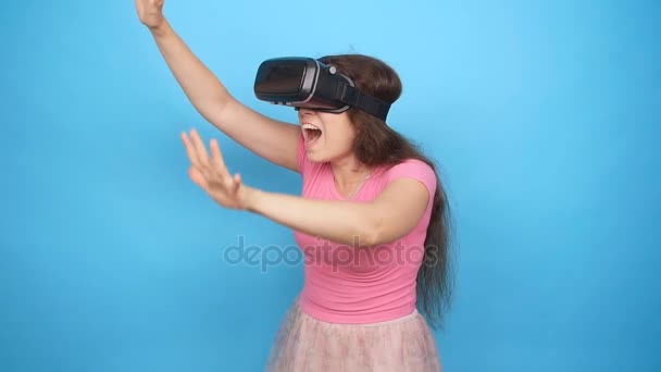 Happy young woman using a virtual reality headset on blue background - Filmmaterial, Video