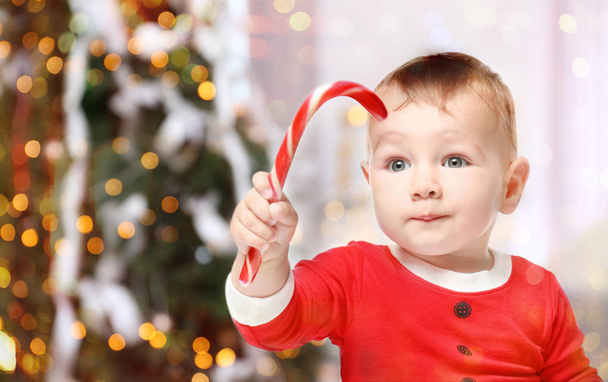 Cute baby with candy cane and Christmas tree on background, Holidays celebration concept - Foto, afbeelding