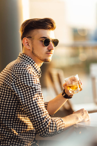 Stylish man sit on the table and drink whiskey - Фото, изображение