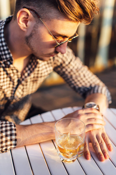 Stylish man sit on the table and drink whiskey - Foto, imagen