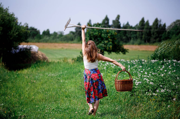 Girl in a bright skirt and wicker basket walks in a green field - Photo, Image
