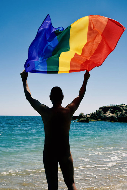homem com uma bandeira do arco-íris na praia
 - Foto, Imagem