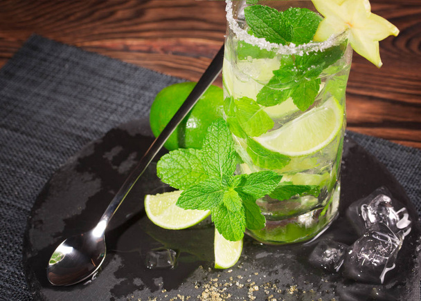 Refreshing mojito with rum, fresh lime, mint, crushed ice and carambola on a dark wooden background. Summer and alcohol beverage. - Photo, Image