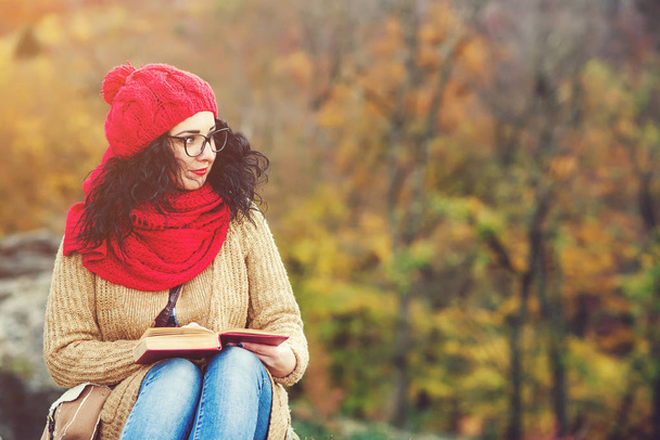 Bella giovane donna che legge un libro in un parco e gode di tempo soleggiato. Stile di vita e concetto autunnale
. - Foto, immagini
