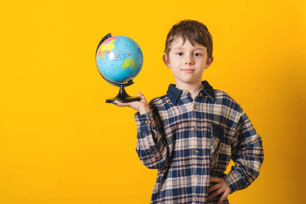 Portrait of little cute boy with globe. Isolated over yellow background. - Photo, Image