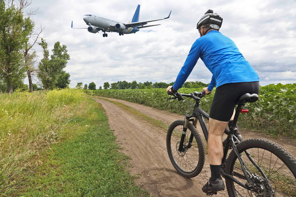 велосипедист едет по тропе на фоне полета пассажирского самолета
 - Фото, изображение