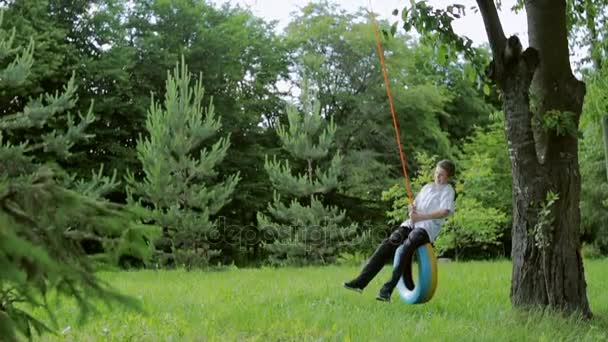 Happy boy swinging on a car tire used as a swing. Concept of childhood, nostalgia, memory, past, life, retro, vintage, home sweet home - Video, Çekim