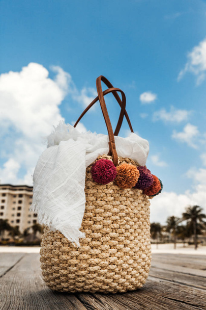 Літня солом'яна сумка з білим шарфом на дерев'яному мосту на пляжі
 - Фото, зображення
