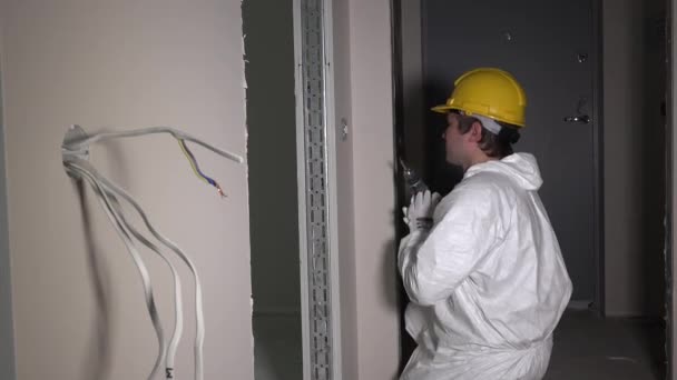 Bauarbeiter schraubt Lichtschalter mit Elektrobohrwerkzeug im Flur - Filmmaterial, Video