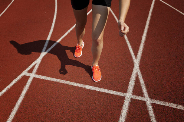 Red running track  with female runner, close up on legs - Фото, изображение