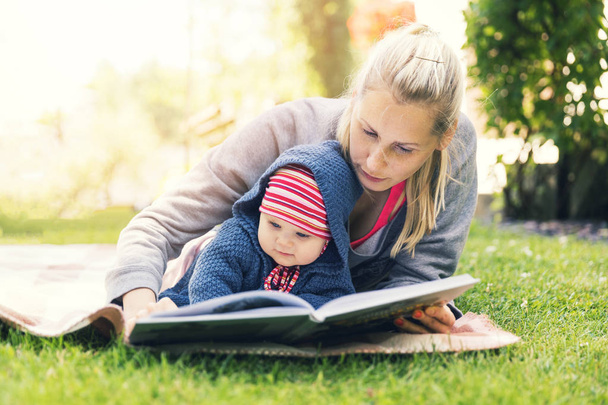 mother reading a book to baby in backyard garden on blanket - Foto, imagen