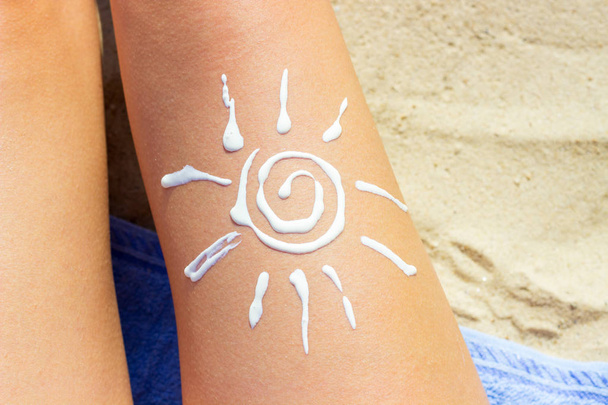 Woman sunbathing on the beach with a drawing of sun on her leg with sunscreen cream - Foto, Imagen