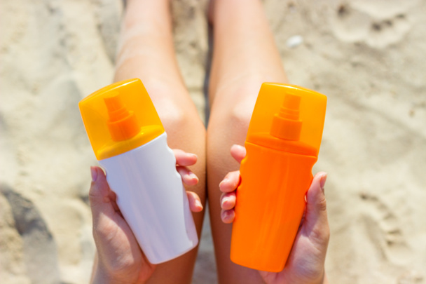 Una mujer sosteniendo dos botellas de protector solar en sus manos. Una chica elige entre dos botellas de protector solar
 - Foto, imagen