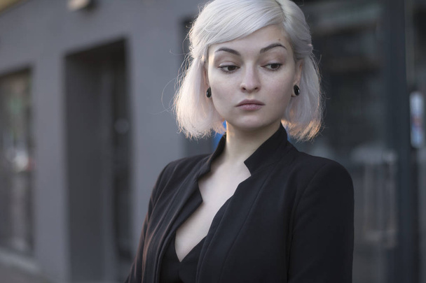 Blond lovely model in sunset light outdoors closeup portrait in black suit and with ear tunnels. no makeup perfect skin. - Photo, Image