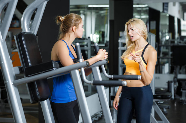 Dwa sportowe kobiet blond, mówi w siłowni. Dziewczyna komunikuje się z trenerem - Zdjęcie, obraz
