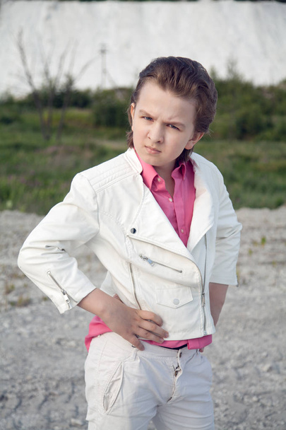 cool white clothes fashion child boy with rude brutal face outdoor near big mountain - Фото, изображение