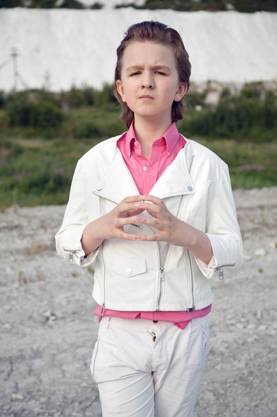 cool white clothes fashion child boy with rude brutal face outdoor near big mountain - Foto, Imagen