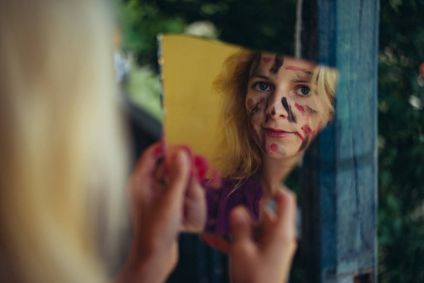 Painted face woman looking at broken mirror - Foto, Bild