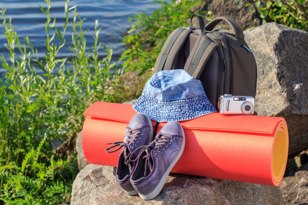 Hiking rugzak, sneakers, hoed, camera en camping mat op rock w - Foto, afbeelding