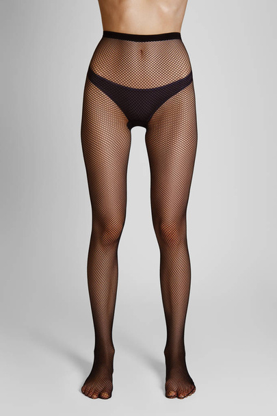 Long slim female legs in elegant and sexy black fishnet tights. Front view. Stand strong. - Φωτογραφία, εικόνα