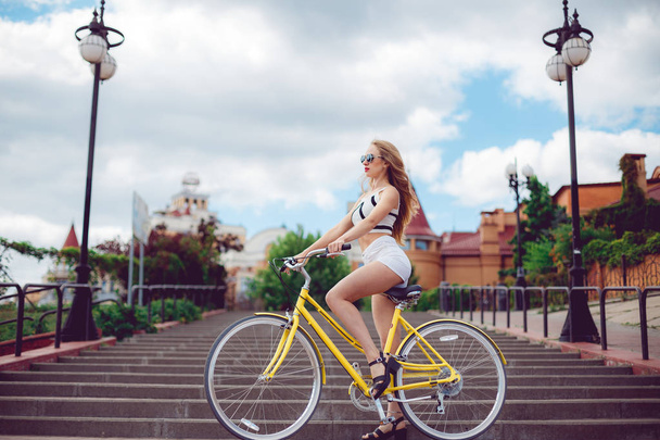 若い美しいヒップ女性白ショート パンツで夏のトレンド スタイルのビーチのそばの自転車に乗って - 写真・画像